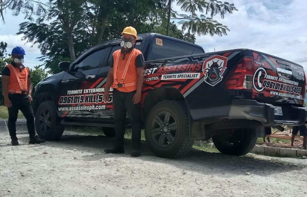 Two Pest Assassins technicians in safety gear beside a branded termite extermination truck, prepared for field operations.