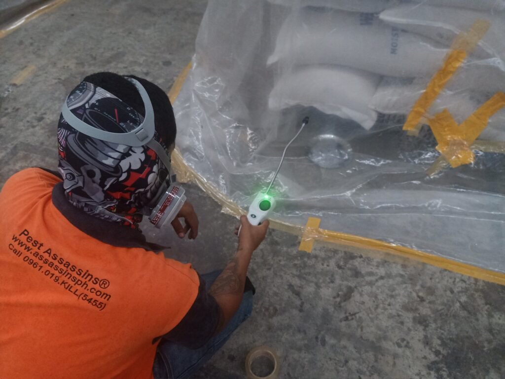 Pest Assassins® technician using a gas detection device to monitor a sealed fumigation zone containing NOBLE-labeled sacks in an industrial setting