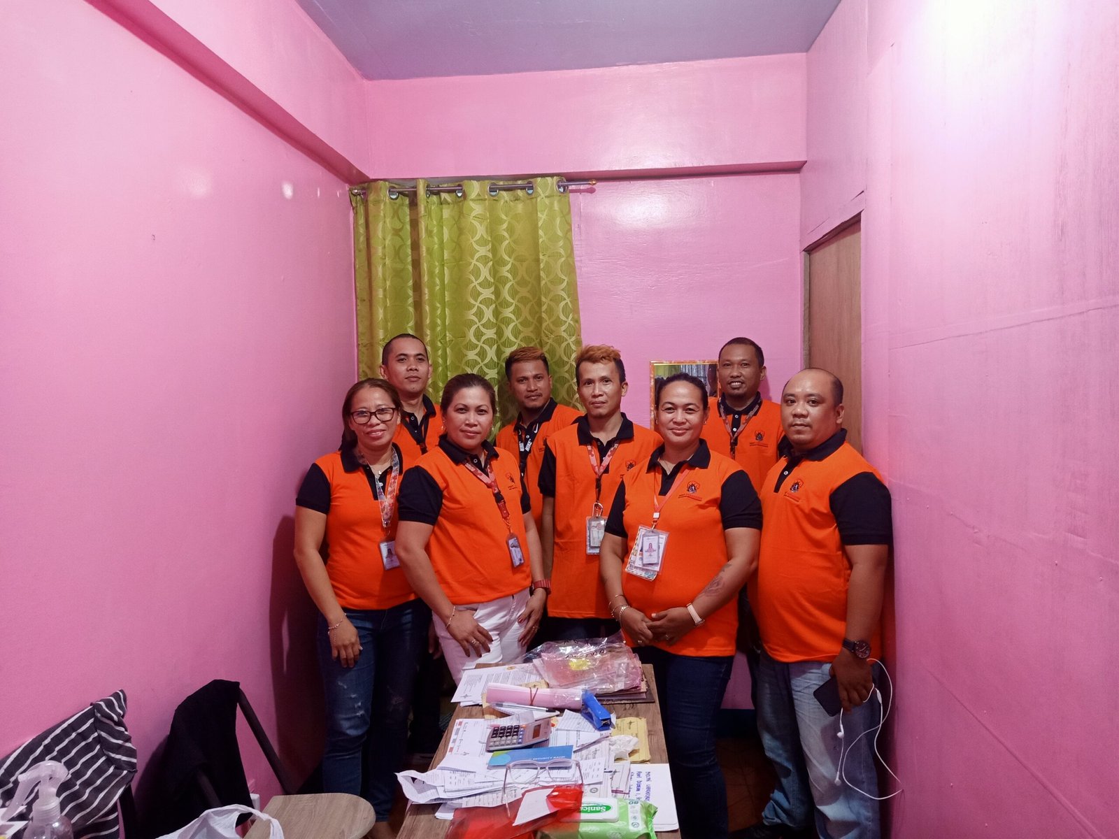 Pest Assassins team members in orange vests posing for a group photo in a small office with administrative materials on the table